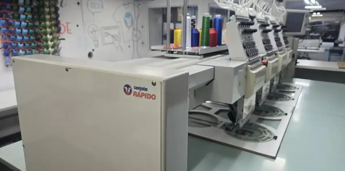 Máquina de bordar industrial Tajima com a marca Camisetas Rápido na fábrica de São Paulo.